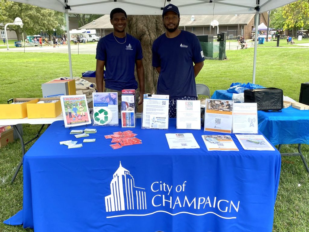 Two Men stand at City of Champaign table with resources.
